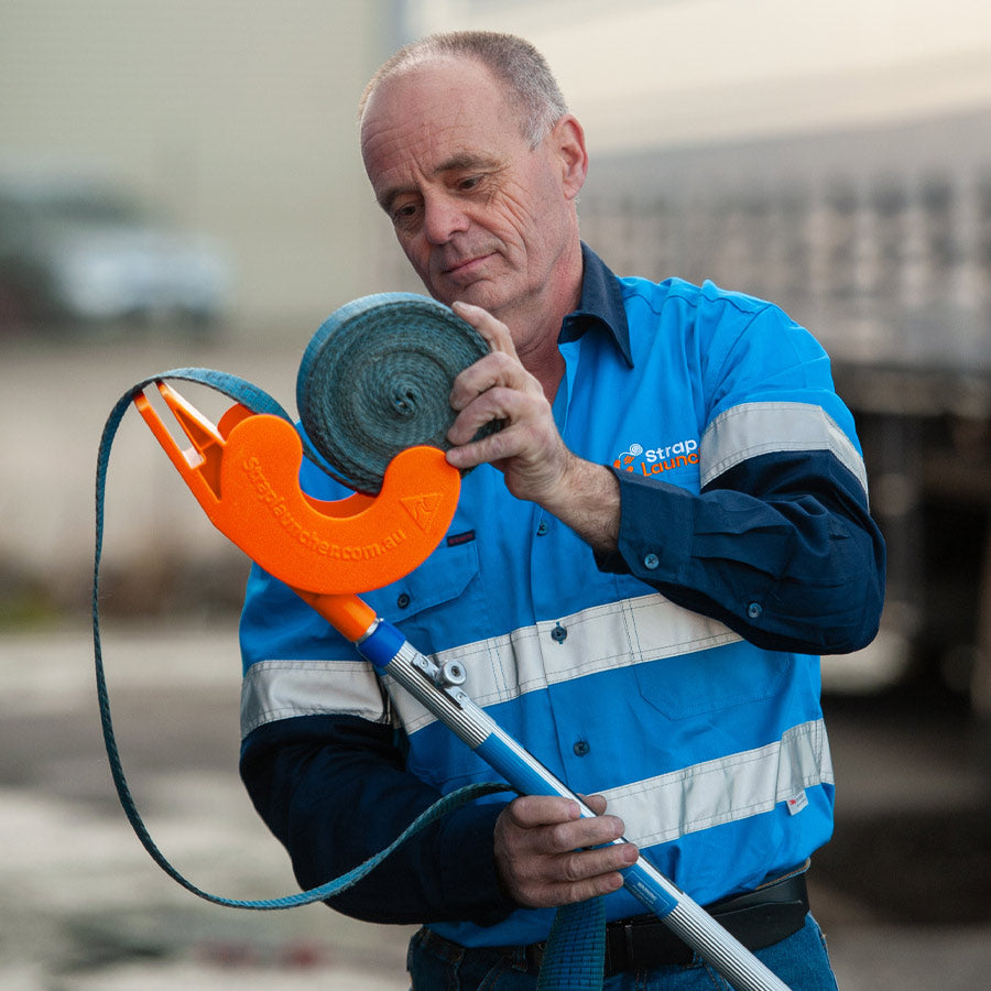 Owen Burns loading a rolled up blue tie-down strap into an orange Strap Launcher tool.